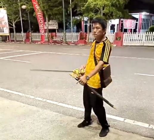 Pria mengenakan kaos kuning dengan garis hitam, celana panjang hitam, memegang samurai di depan Mess Pemda Rokan Hili
